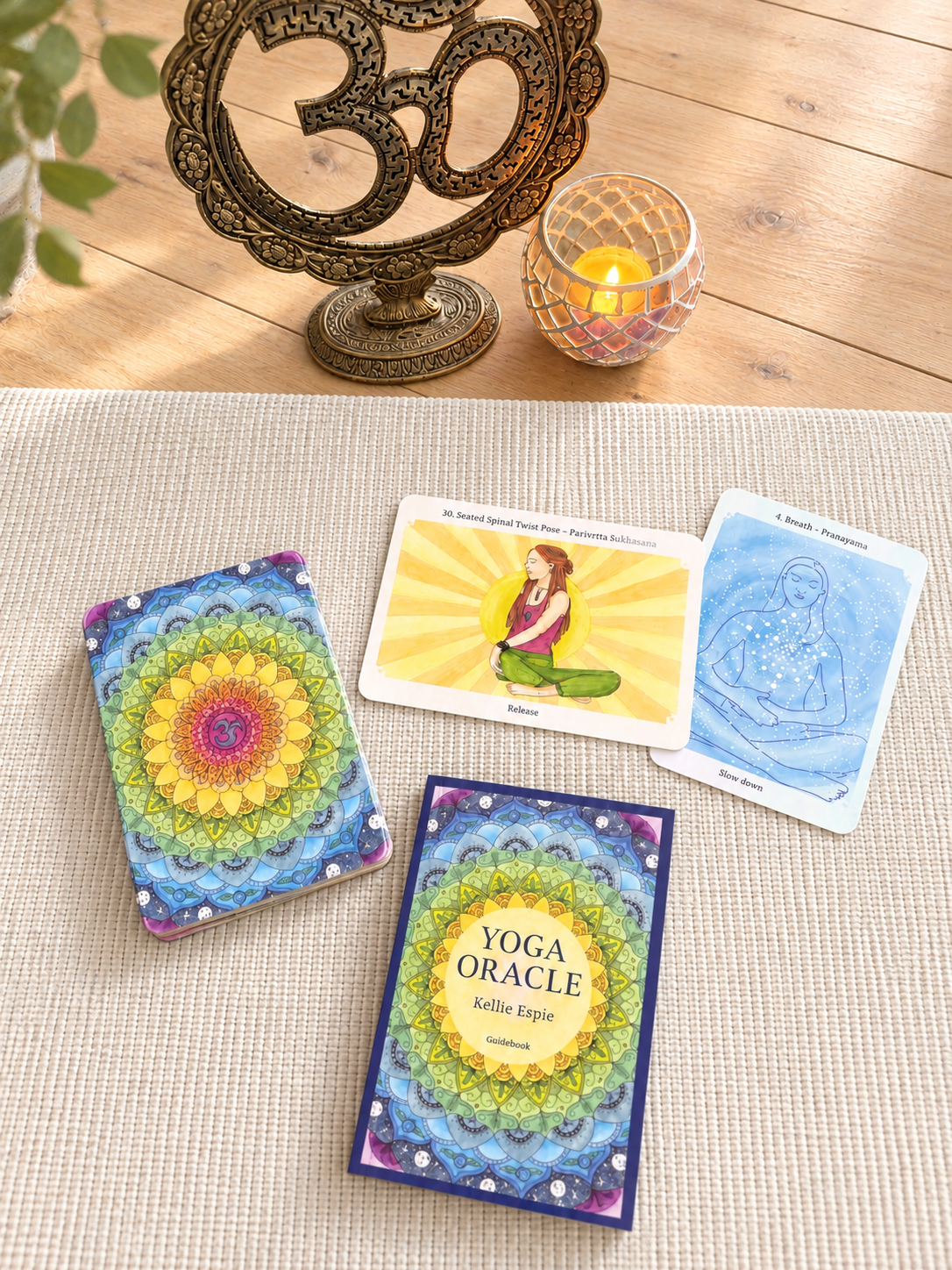 Yoga Oracle deck, guidebook and cards arranged with an Om statue and candle